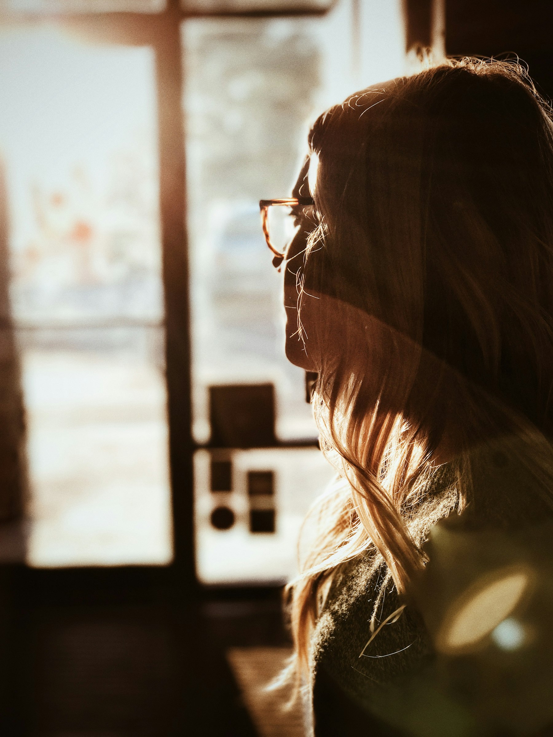 Mujer adulta mirando por la ventana con luz cálida