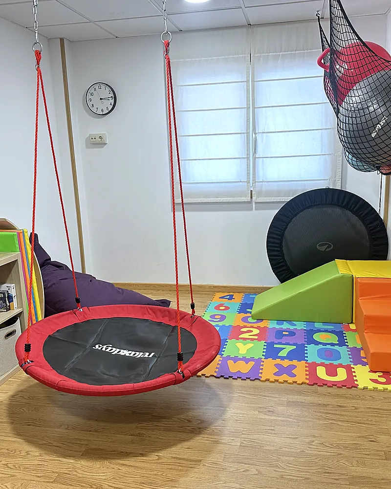 Sala de terapia ocupacional y fisioterapia con columpio nido, cama elástica y bloques de psicomotricidad