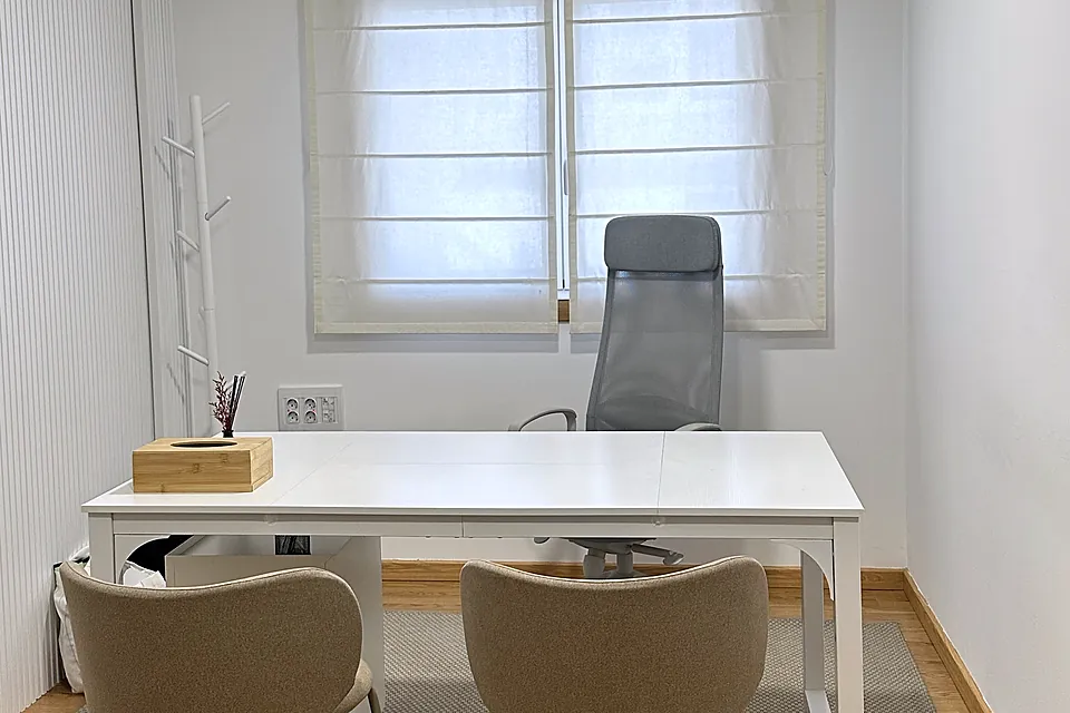 Consulta con mesa blanca, dos sillas tapizadas y ventana con estor