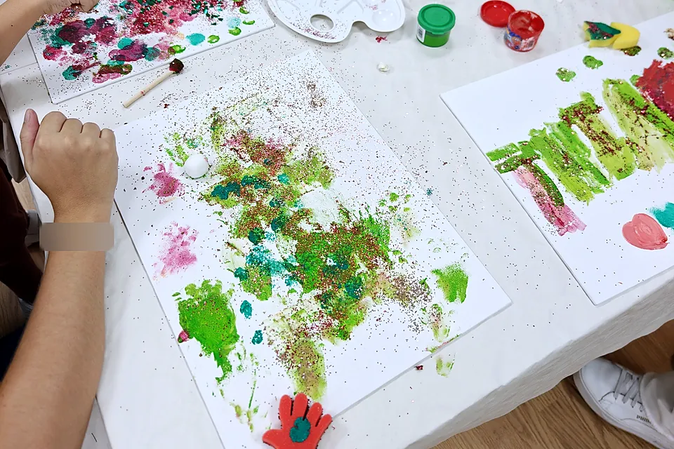 Mesa del taller vista desde arriba, con manos pintando cuadros de colores